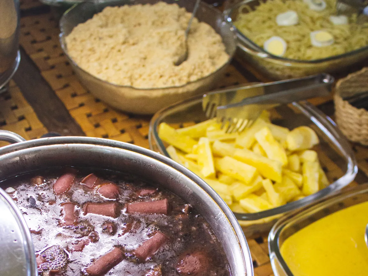 Mesa do jantar servida, com a panela de feijoada, farofa, mandioca frita e creme de milho