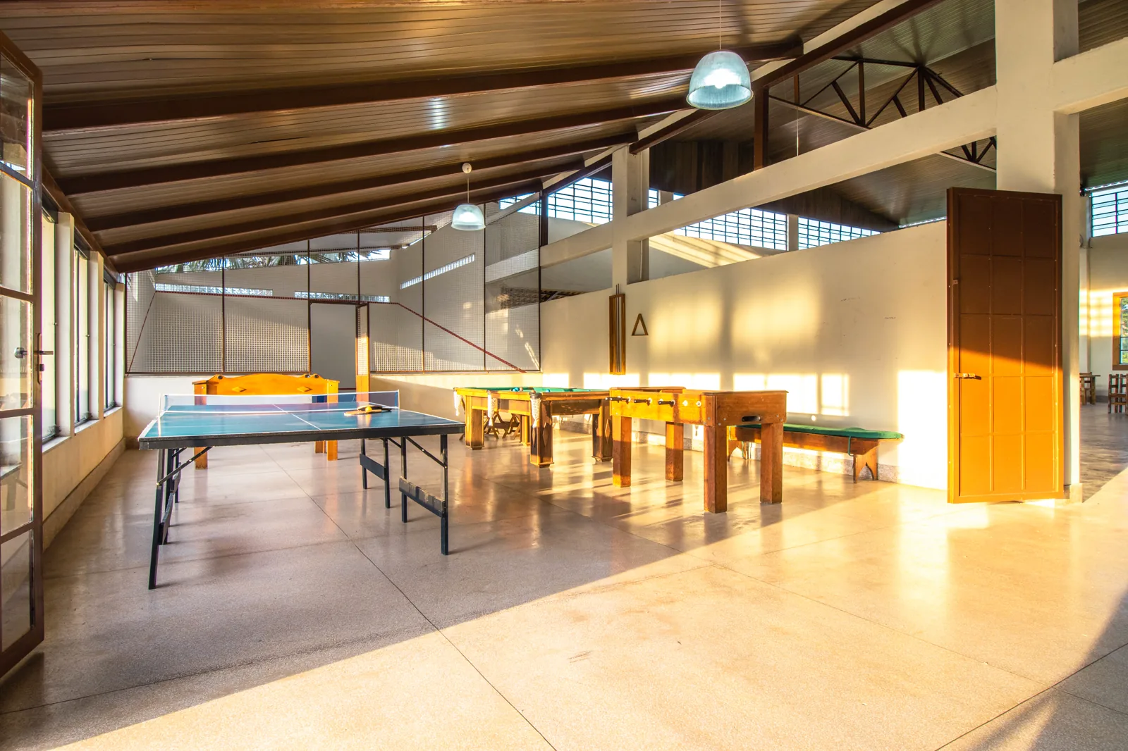 Salão de jogos do Hotel Fazenda Minas Real visto de ponta a ponta, com as mesas de tênis de mesa e pebolim